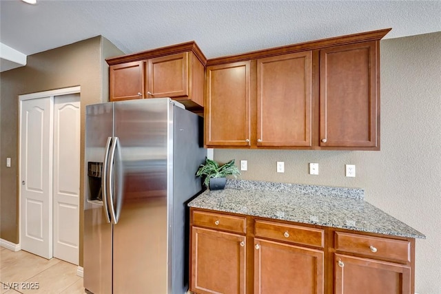 kitchen with brown cabinetry, light stone counters, stainless steel refrigerator with ice dispenser, and light tile patterned flooring