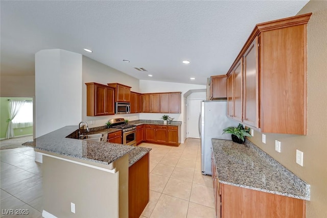 kitchen featuring a peninsula, appliances with stainless steel finishes, light stone counters, and a sink