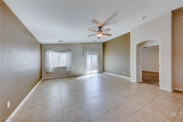 empty room featuring light tile patterned floors, visible vents, arched walkways, ceiling fan, and vaulted ceiling