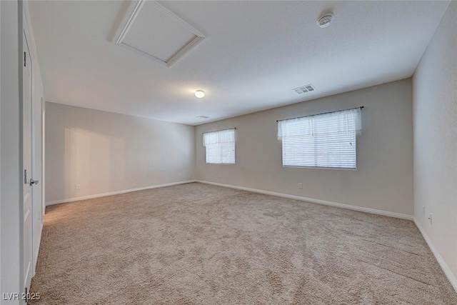 carpeted empty room with attic access, visible vents, and baseboards