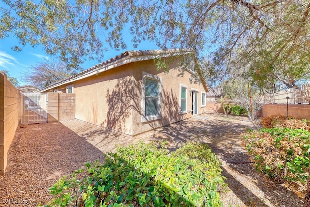 back of house with a fenced backyard, a gate, a patio, and stucco siding