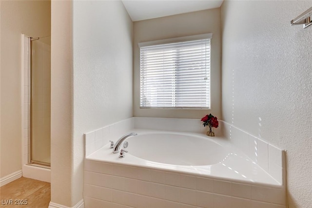 full bathroom featuring a stall shower, a garden tub, and a textured wall