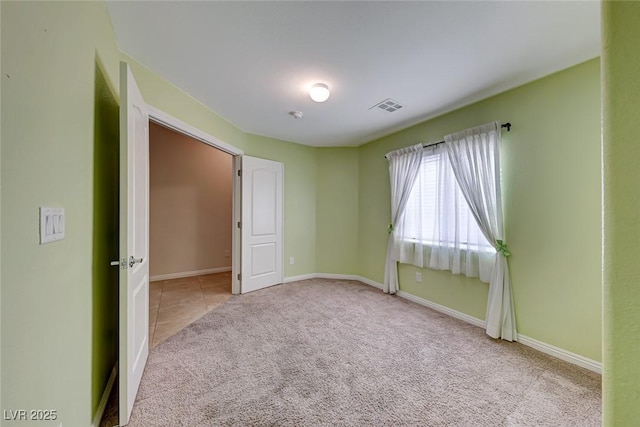 carpeted spare room with visible vents, baseboards, and tile patterned floors