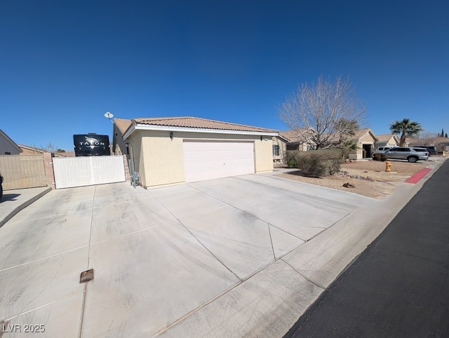 exterior space with concrete driveway, a tiled roof, an attached garage, a gate, and stucco siding