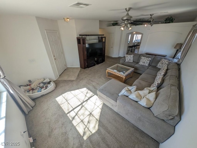 living room featuring a ceiling fan, light colored carpet, visible vents, and arched walkways