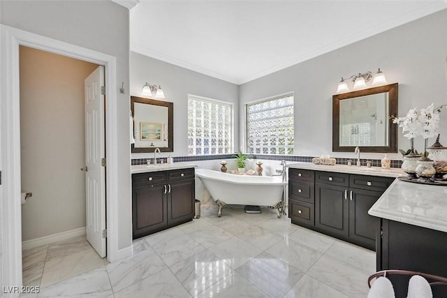 full bathroom featuring marble finish floor, two vanities, ornamental molding, a sink, and a freestanding tub