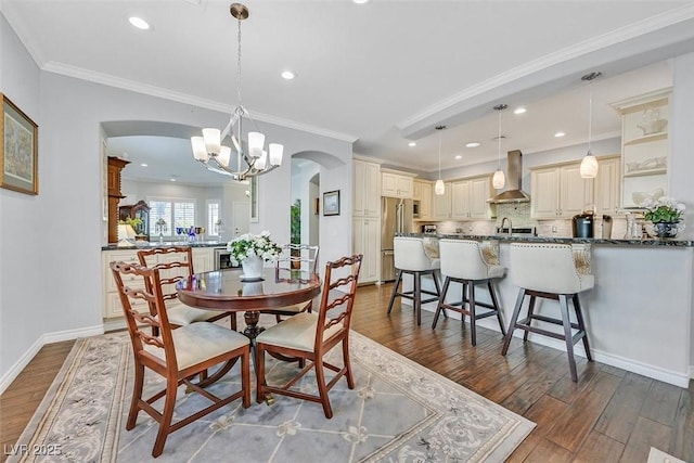 dining area with arched walkways, a notable chandelier, wood finished floors, baseboards, and ornamental molding