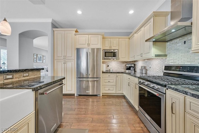 kitchen with stainless steel appliances, light wood-style flooring, wall chimney range hood, and cream cabinets