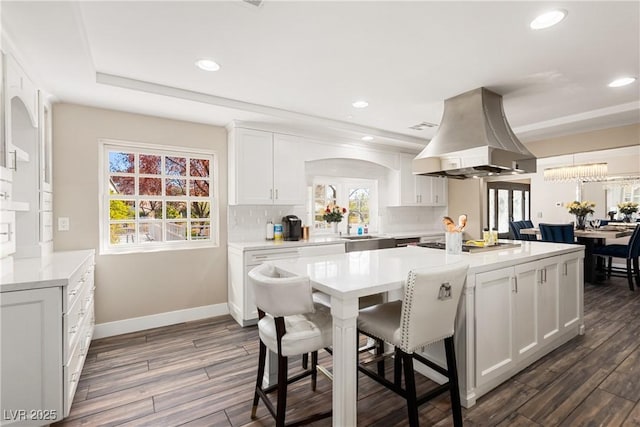 kitchen with white cabinets, decorative backsplash, island exhaust hood, a kitchen bar, and a sink