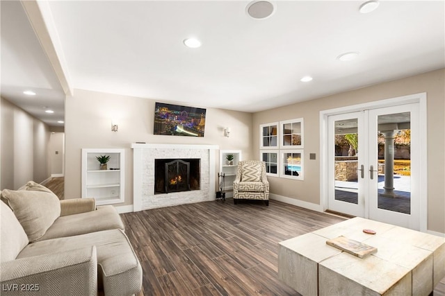 living area with dark wood-type flooring, a warm lit fireplace, french doors, and recessed lighting