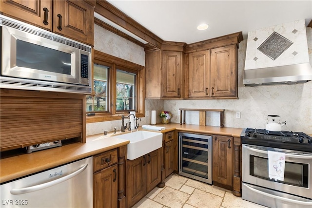 kitchen featuring wine cooler, stone tile floors, a sink, appliances with stainless steel finishes, and wall chimney exhaust hood