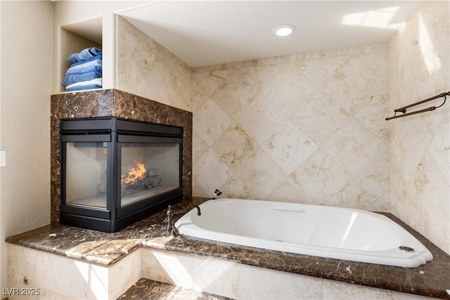 bathroom featuring a garden tub, tile walls, and a multi sided fireplace