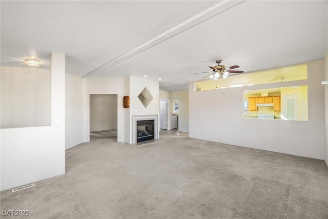 unfurnished living room with ceiling fan, carpet floors, a fireplace with flush hearth, and visible vents