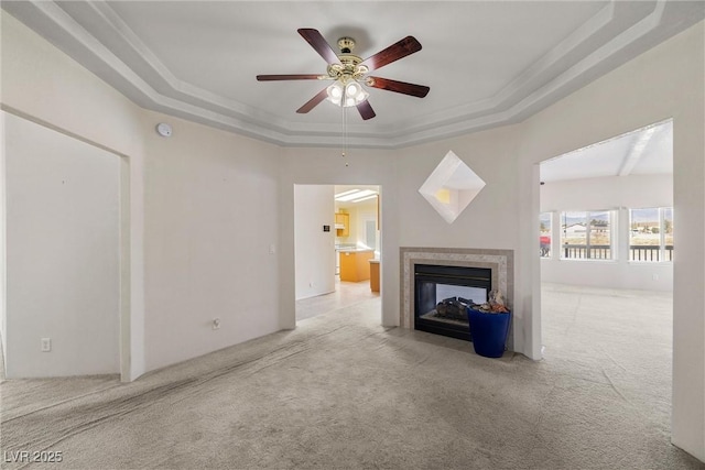 unfurnished living room featuring carpet, a tiled fireplace, a raised ceiling, and a ceiling fan