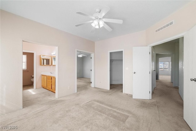 unfurnished bedroom featuring a closet, light colored carpet, visible vents, a spacious closet, and ensuite bath