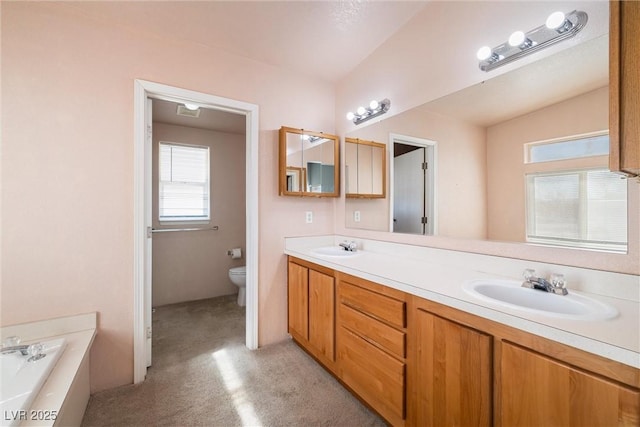 bathroom featuring a garden tub, double vanity, a sink, and toilet