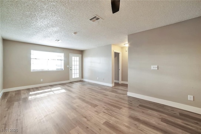 unfurnished room with baseboards, visible vents, light wood finished floors, and a textured ceiling