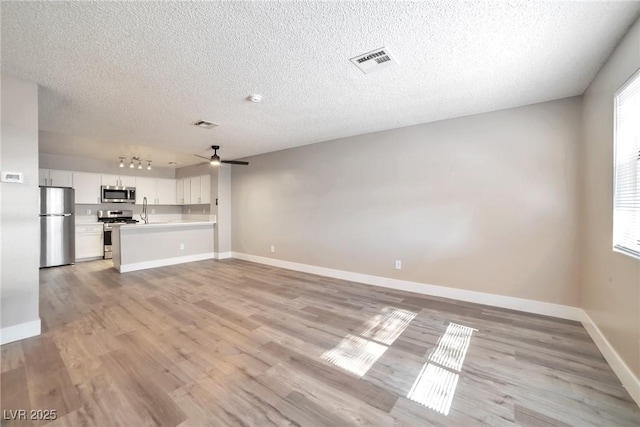 unfurnished living room featuring visible vents, light wood-type flooring, a sink, baseboards, and ceiling fan