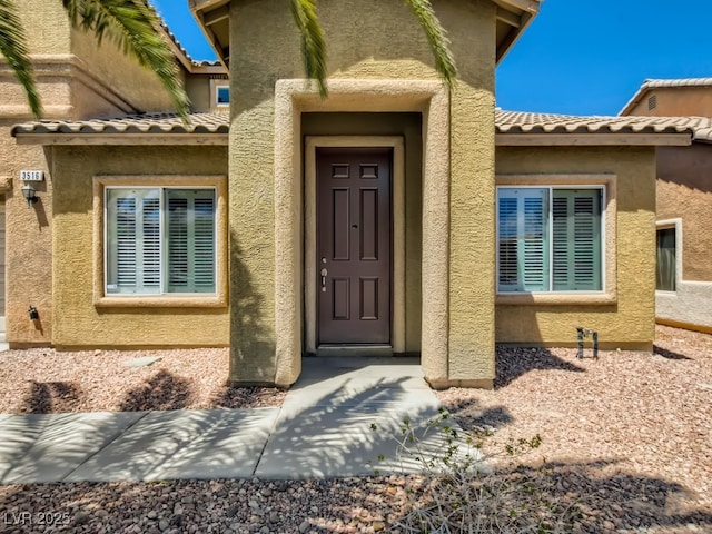 view of exterior entry with a tiled roof and stucco siding