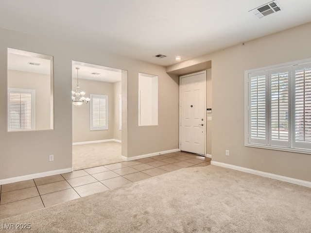 carpeted empty room featuring a chandelier, visible vents, baseboards, and tile patterned floors