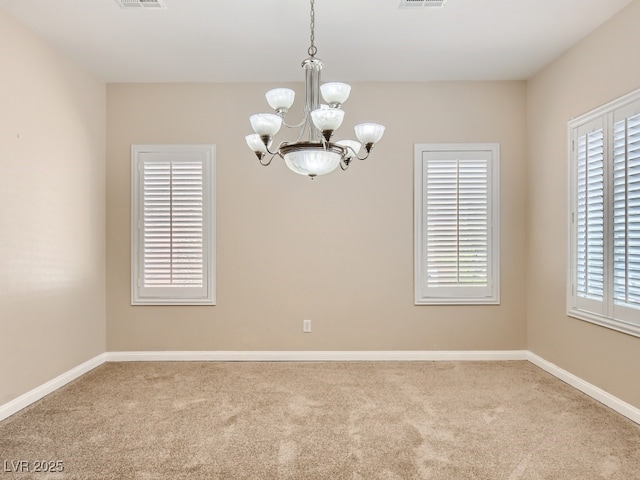 carpeted empty room featuring baseboards, visible vents, and a notable chandelier