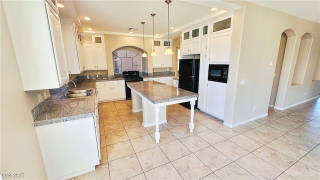 kitchen with arched walkways, white cabinets, a kitchen island, black appliances, and a sink