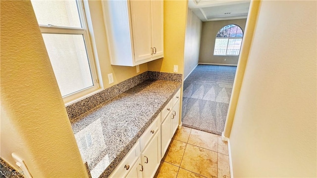 kitchen featuring stone counters, white cabinetry, light carpet, light tile patterned flooring, and baseboards