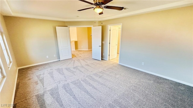 unfurnished bedroom featuring light colored carpet, connected bathroom, baseboards, and ceiling fan