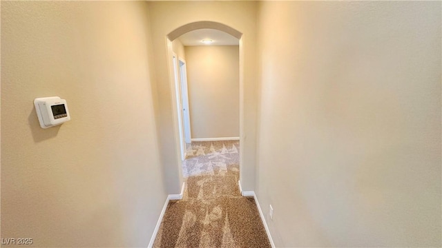 corridor with arched walkways, carpet, and baseboards