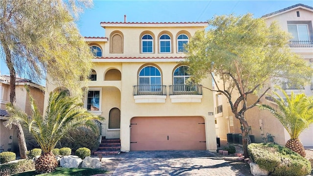 mediterranean / spanish-style home featuring decorative driveway, a tile roof, stucco siding, central AC, and a garage