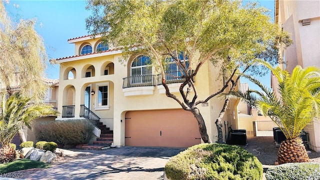 mediterranean / spanish home with a garage, stairs, a tiled roof, decorative driveway, and stucco siding