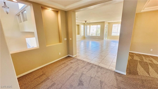 carpeted empty room featuring ceiling fan, baseboards, and tile patterned floors