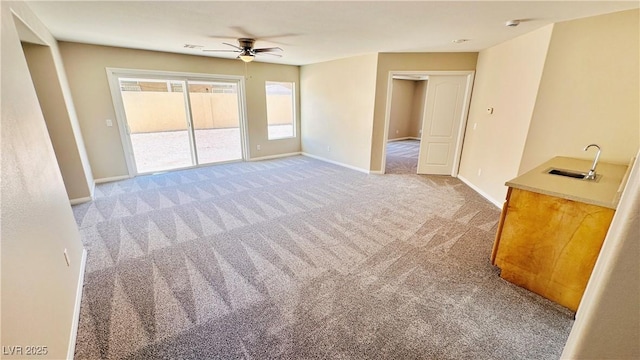 interior space featuring baseboards, a sink, a ceiling fan, and light colored carpet