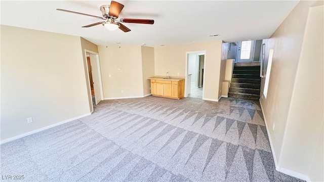 unfurnished living room featuring light colored carpet, ceiling fan, a sink, baseboards, and stairs