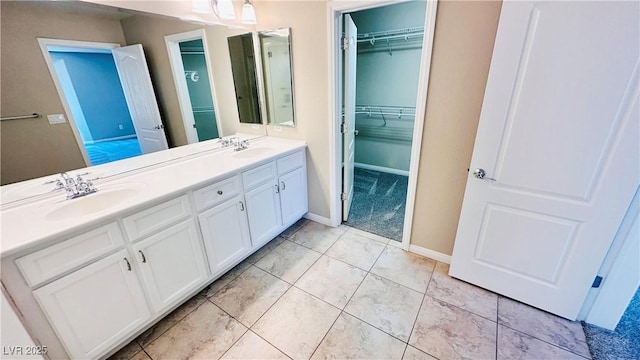 bathroom with double vanity, a walk in closet, a sink, and tile patterned floors