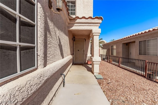 view of exterior entry with fence and stucco siding