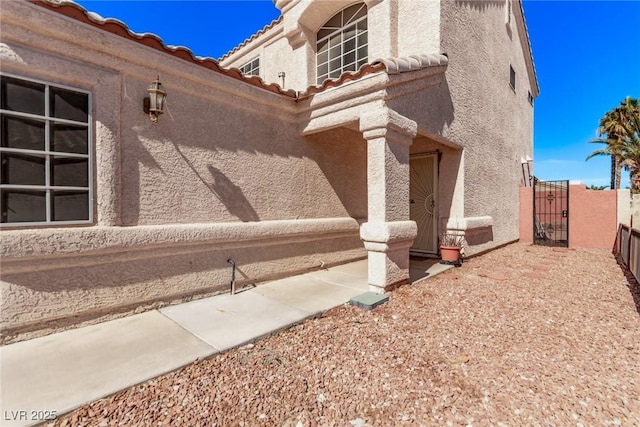 view of side of home with fence, a tile roof, a gate, and stucco siding