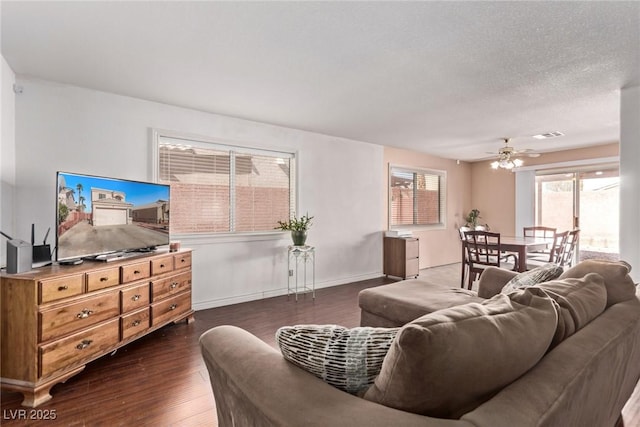 living room featuring a textured ceiling, dark wood-type flooring, visible vents, a ceiling fan, and baseboards