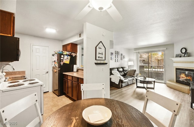 dining area with a textured ceiling, a tiled fireplace, visible vents, and a ceiling fan