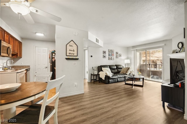 living area featuring light wood-style flooring, baseboards, ceiling fan, and a textured ceiling