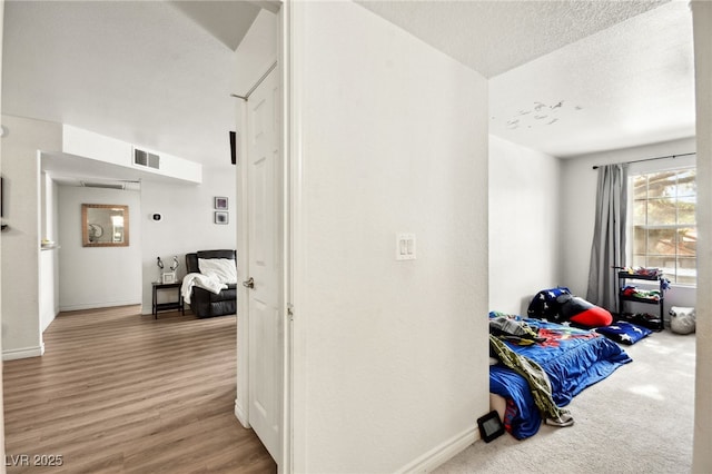 corridor with visible vents, a textured ceiling, baseboards, and wood finished floors