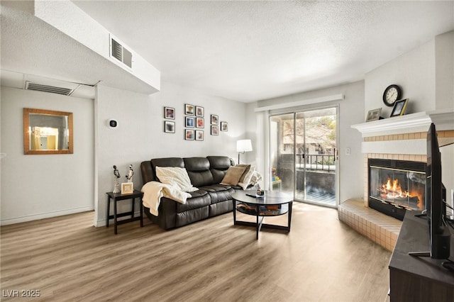 living room featuring a brick fireplace, a textured ceiling, visible vents, and wood finished floors