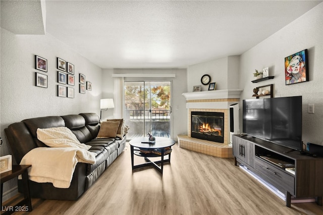 living room featuring light wood-type flooring, a textured wall, a textured ceiling, and a tiled fireplace