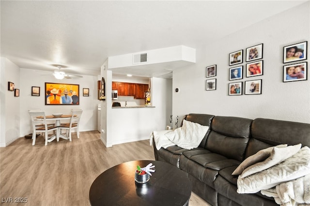 living area with a ceiling fan, light wood-type flooring, visible vents, and baseboards