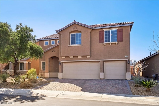 mediterranean / spanish-style house featuring decorative driveway, an attached garage, a tile roof, and stucco siding