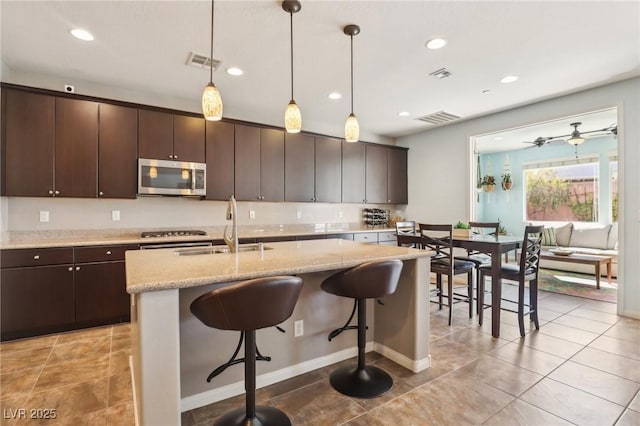 kitchen featuring visible vents, stainless steel microwave, a breakfast bar, and a sink