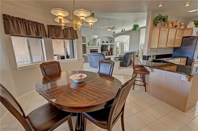 dining area featuring arched walkways, ceiling fan with notable chandelier, a fireplace, and light tile patterned flooring