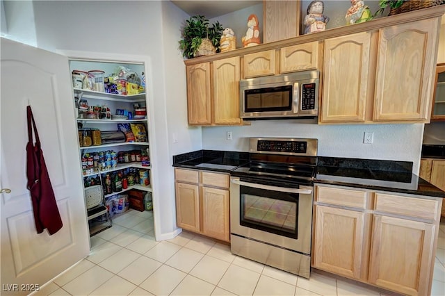 kitchen with light brown cabinets, appliances with stainless steel finishes, and dark stone countertops