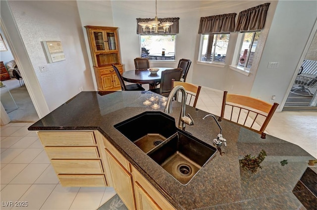 kitchen featuring light tile patterned floors, hanging light fixtures, light brown cabinetry, a sink, and dark stone counters