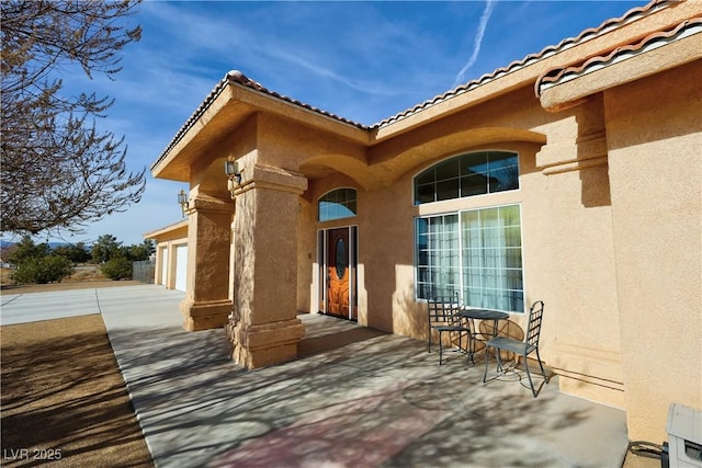 entrance to property with driveway, an attached garage, a tile roof, and stucco siding